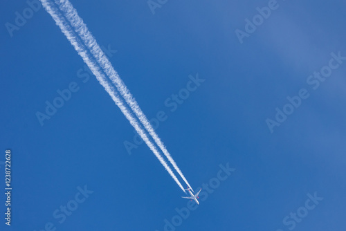 Ein Verkehrsflugzeug fliegt hoch am Himmel und hinterlässt zwei lange, weiße Kondensstreifen vor einem klaren blauen Himmel.