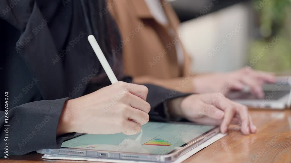 A woman is writing on a tablet with a white pen. The tablet is on a wooden table A woman is writing on a tablet with a white pen. The tablet is on a wooden table