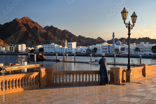 The Muttrah corniche viewed from the esplanade next to the fish market at sunset, with an Omani man traditionally dressed and the mosque and mountains in the background, Muttrah, Muscat, Oman