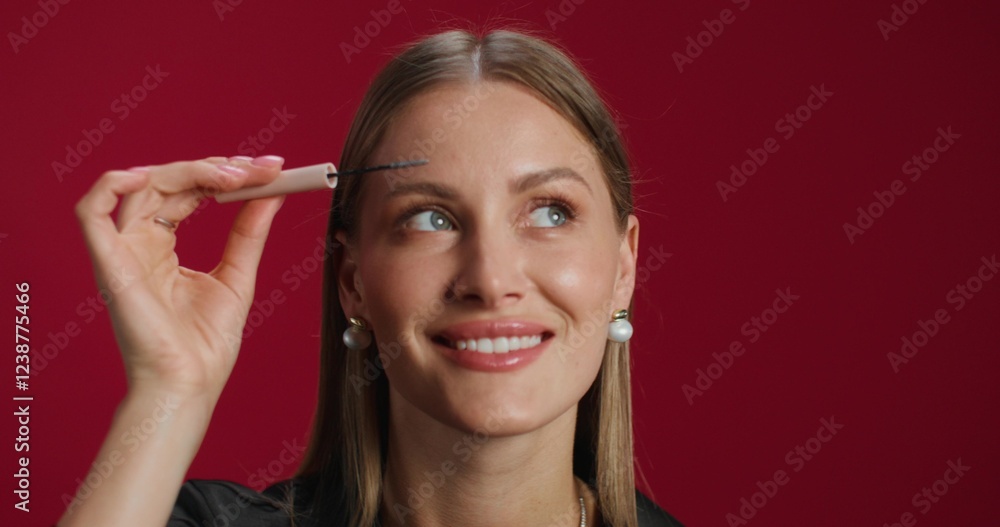A woman applies gel to her eyebrows. She smiles at the camera standing in the studio background. Close-up of her face A woman applies gel to her eyebrows. She smiles at the camera standing in the studio background. Close-up of her face