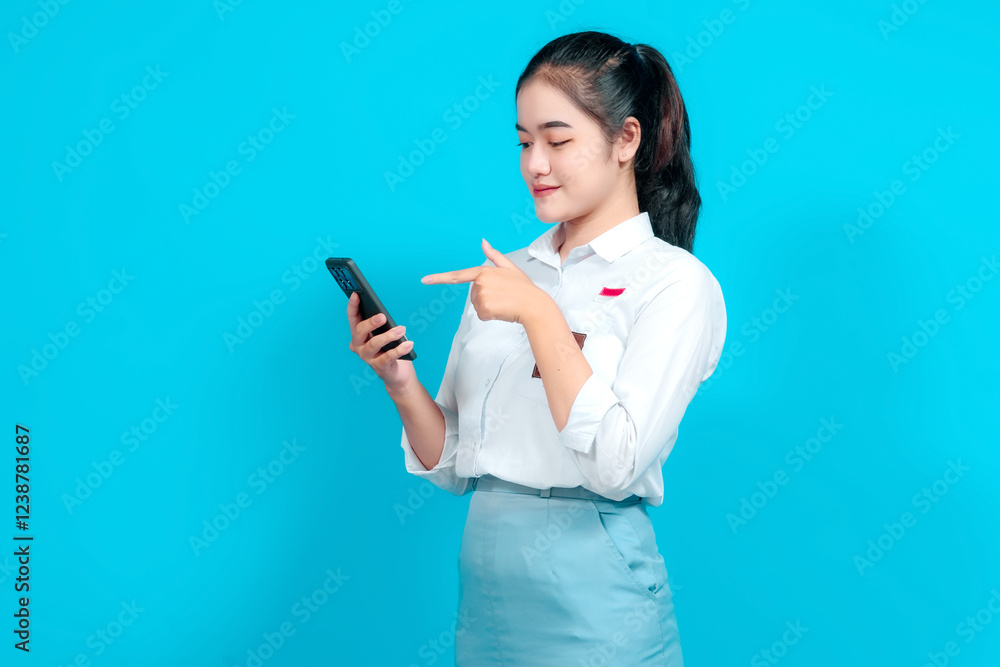 Smiling female student dressed in a uniform pointing while holding a smartphone Smiling female student dressed in a uniform pointing while holding a smartphone