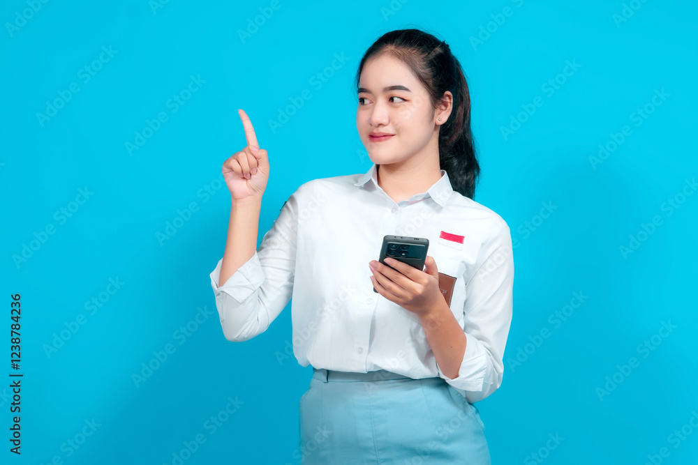 Smiling female student dressed in a uniform pointing while holding a smartphone Smiling female student dressed in a uniform pointing while holding a smartphone