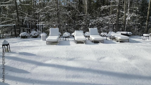 aerial view of snow covered lounge chairs next to closed shuttered swimming pool in winter (back yard patio loungers outdoor furniture) spa bizzard snowy snowfall frozen home countryside drone footage