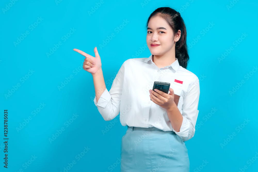 Smiling female student dressed in a uniform pointing while holding a smartphone Smiling female student dressed in a uniform pointing while holding a smartphone