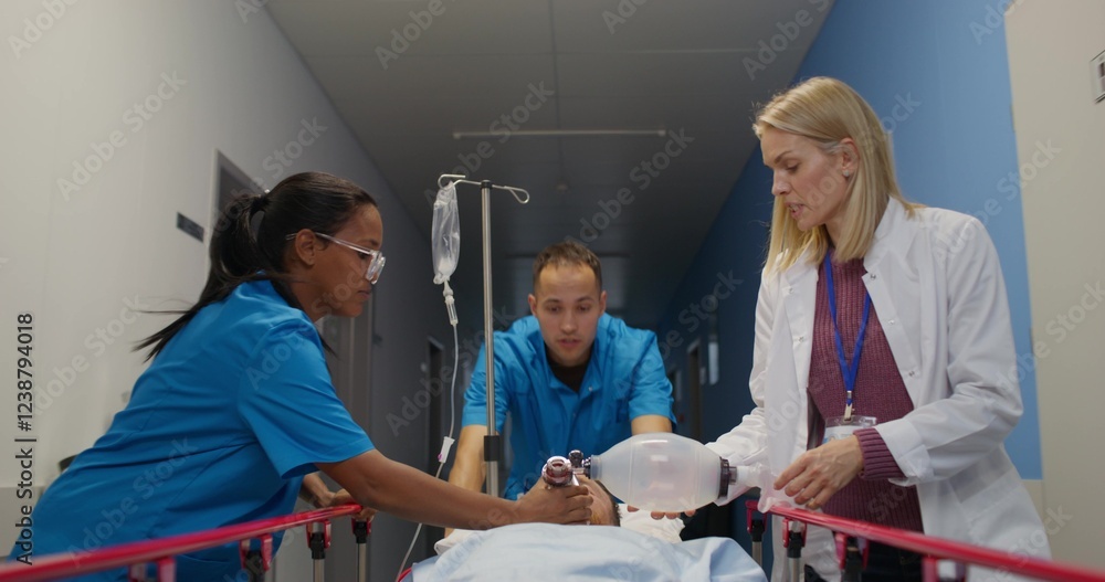 Obraz premium Medical workers carry a patient on a gurney along the hospital corridor. A woman holds an oxygen mask near his face