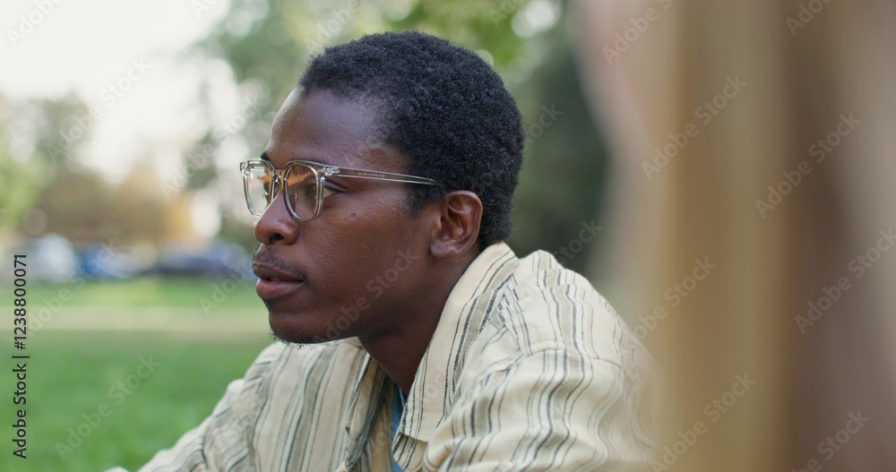 A man is talking to his friends while sitting on the grass in the park. Sunny summer day A man is talking to his friends while sitting on the grass in the park. Sunny summer day