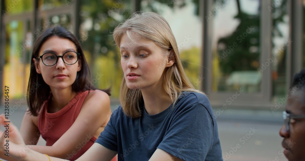 A group of young people are talking while repeating lessons while sitting on the steps of the university. A woman holds cards with a summary in her hands. A group of young people are talking while repeating lessons while sitting on the steps of the university. A woman holds cards with a summary in her hands.