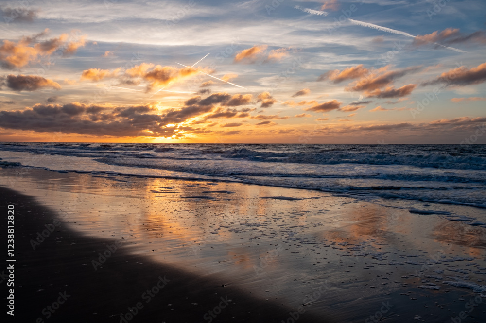 A beautiful sunset casts colorful hues on ocean waves, reflecting brilliantly on the wet beach sand A beautiful sunset casts colorful hues on ocean waves, reflecting brilliantly on the wet beach sand