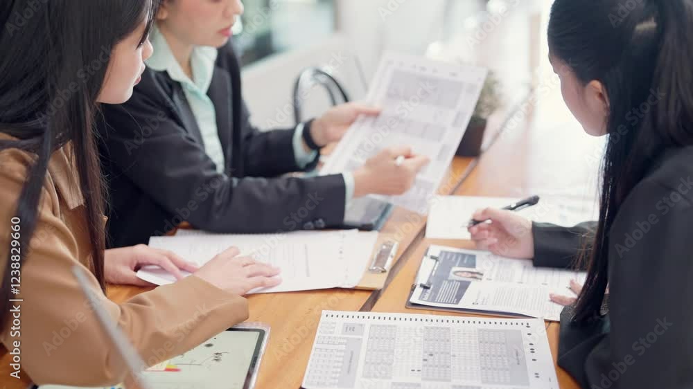 Three women are sitting at a table with papers in front of them. They are discussing something important Three women are sitting at a table with papers in front of them. They are discussing something important