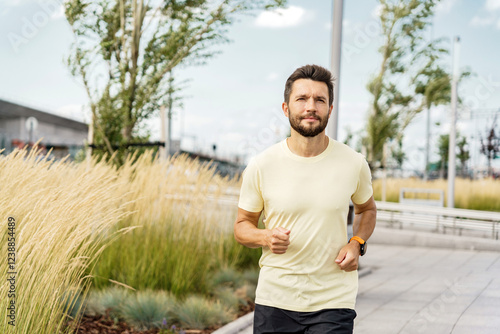 Man jogging in a modern park setting with tall grass, showcasing fitness and leisure during daytime photo