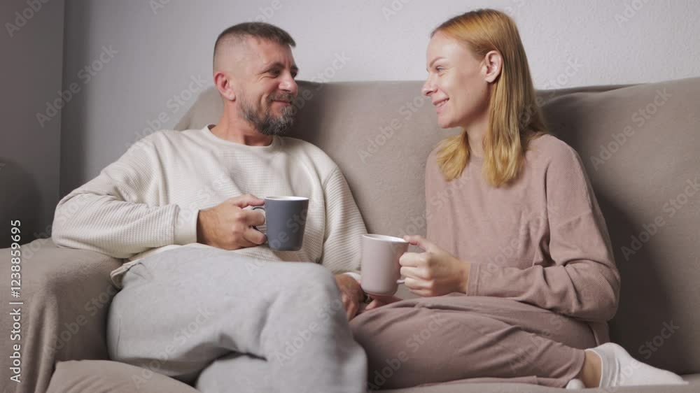 Affectionate couple relaxing on neutral sofa, sipping hot drinks, sharing soft conversation and tender connection in cozy home environment. Affectionate couple relaxing on neutral sofa, sipping hot drinks, sharing soft conversation and tender connection in cozy home environment.