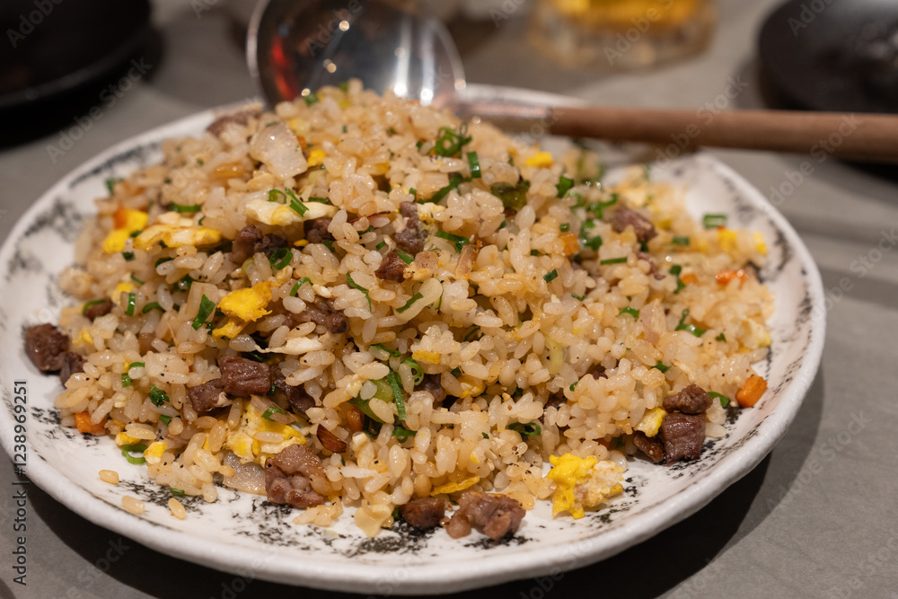 A plate of flavorful fried rice with diced beef, scrambled eggs, green onions, and vegetables, served on a white dish with a spoon. A plate of flavorful fried rice with diced beef, scrambled eggs, green onions, and vegetables, served on a white dish with a spoon.