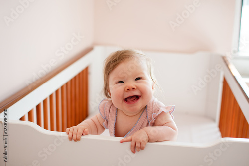 Cute Caucasian baby girl laughing standing in her crib. Portrait of laughing happy healthy 7 month old baby girl photo