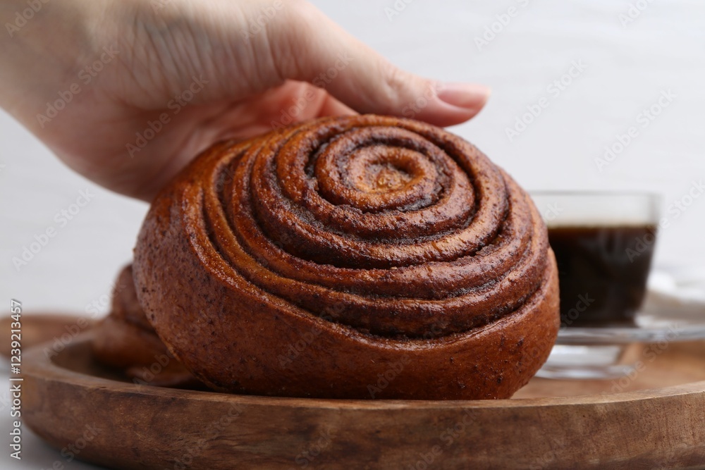 Woman taking delicious cinnamon roll from board at table, closeup Woman taking delicious cinnamon roll from board at table, closeup
