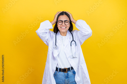 Young brunette doctor woman wearing stethoscope standing over isolated yellow background suffering from headache desperate and stressed because pain and migraine with her hands on head
