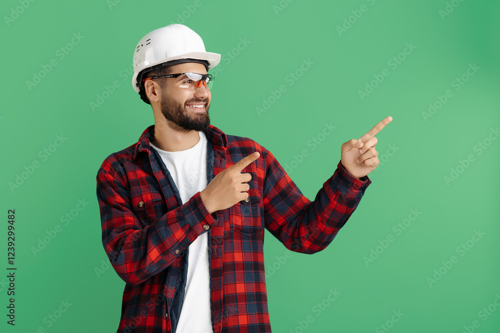 Handsome bearded engineer or constructor man in casual outfit pointing finger away over green background Handsome bearded engineer or constructor man in casual outfit pointing finger away over green background