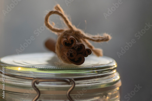 Obraz na płótnie Fresh raw cinnamon sticks on glass dose bottle, sticks tied with one jute natural twines w salonie