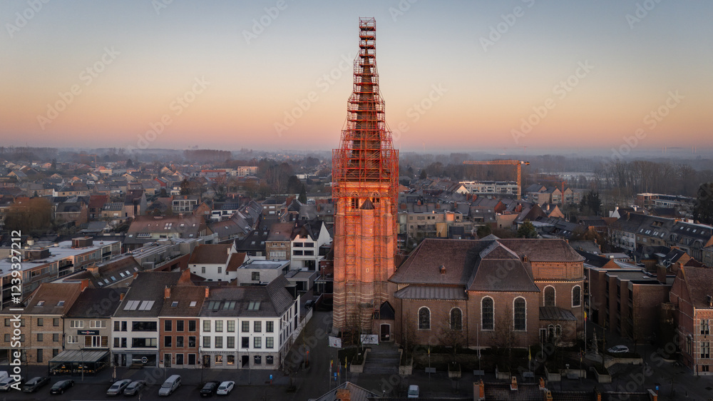 Fototapeta premium aerial view, drone view of the Sint-Servatiuskerk church in Diepenbeek, Belgium. The tower is standing in construction scaffolding for renovation of the tower. Early morning sunrise during winter.