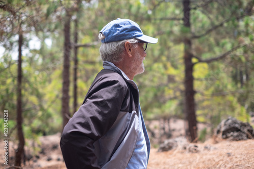 Side view of active senior man with cap walking in a mountain forest enjoying nature, freedom and ealthy lifestyle photo