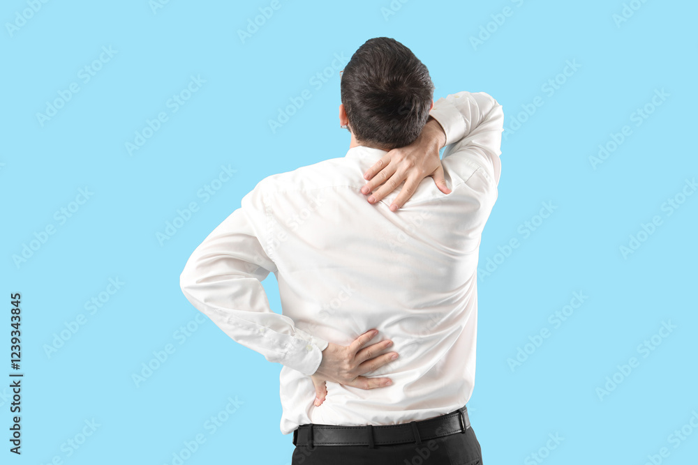 Young businessman suffering from back pain on blue background Young businessman suffering from back pain on blue background