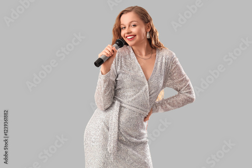 Beautiful woman with microphone singing karaoke on light background