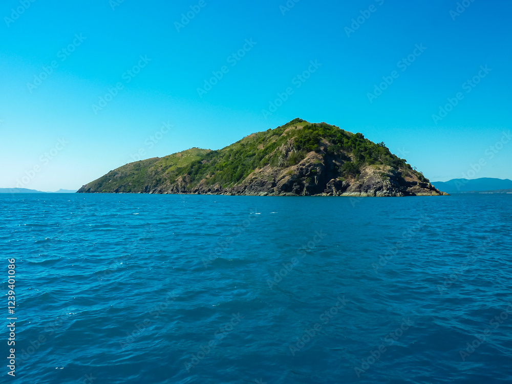 Naklejka premium Rugged mountainous island rising from crystal-clear turquoise waters in the Whitsundays archipelago, Queensland, Australia. Pristine natural beauty of the Coral Sea. Remote secluded island
