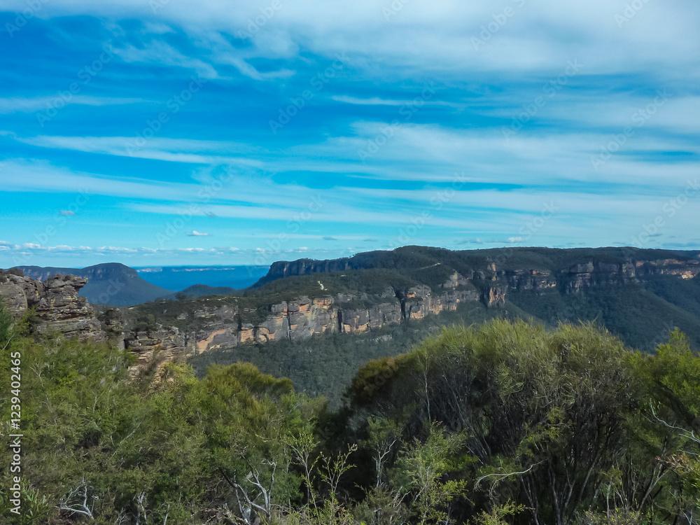 Fototapeta premium Panoramic view of Blue Mountains National Park in Australia. Deep valleys, dramatic sandstone cliffs, and eucalyptus forests under a pristine blue sky. Majestic mountain ranges stretching to horizon
