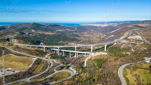 A stunning aerial drone view of Črni Kal, Slovenia, featuring the historic Castle of San Sergio atop a hill and the modern Črni Kal Viaduct, part of the A1 motorway (toll road), spanning Vipava Valley