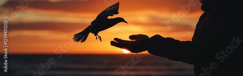 A person stands at the beach, silhouetted against a vibrant sunrise, gently letting a bird take flight. This moment captures themes of freedom and the beauty of new beginnings photo