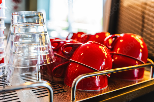 Many ceramic red coffee cups on a coffee machine shelf in a cafe. Selective focus. Red coffee cups on a shelf in a cafe, second row of selective red cup with soft focus. photo