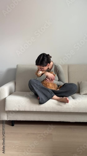 Girl petting and teasing cute ginger cat sitting on the sofa at home