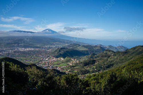 Snow-capped peak overlooking lush green valleys and a coastal town in Tenerife, Canary Islands.