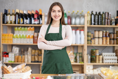 Portrait of positive female seller in an apron behind the counter of a grocery store