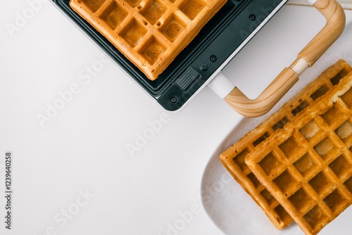 Golden waffles on a white plate with a waffle iron on a light background. Freshly baked crispy breakfast food with a delicious texture. Minimalistic composition with warm tones photo