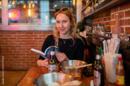 Woman enjoys a moment of peace, reading a book at a cozy restaurant, surrounded by delicious food and drink.