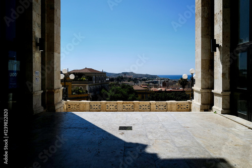 A breathtaking view of the city and sea unfolds from a sun-drenched stone terrace on a clear summer day.