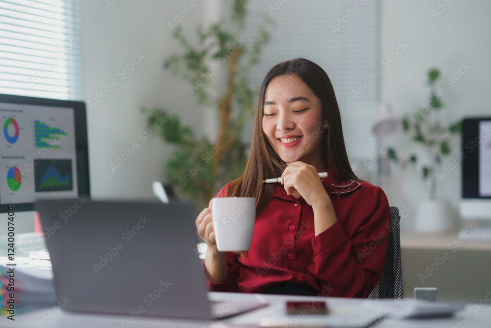 Asian businesswoman drinking coffee and working on laptop in modern office Asian businesswoman drinking coffee and working on laptop in modern office