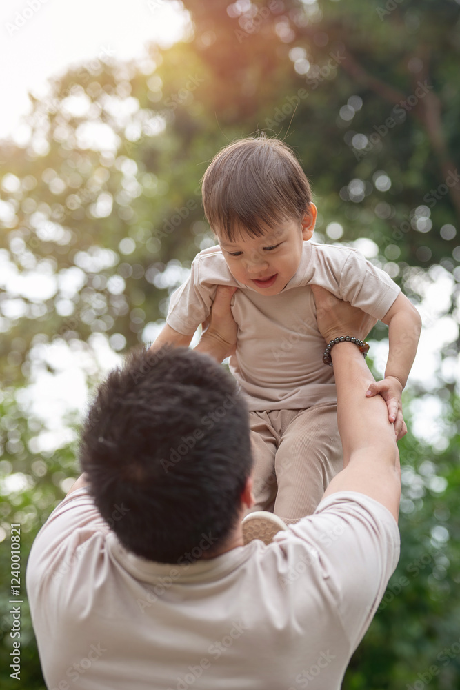 An innocent little Asian boy smiles as his dad lifts him into the air, enjoying a fun time together. An innocent little Asian boy smiles as his dad lifts him into the air, enjoying a fun time together.