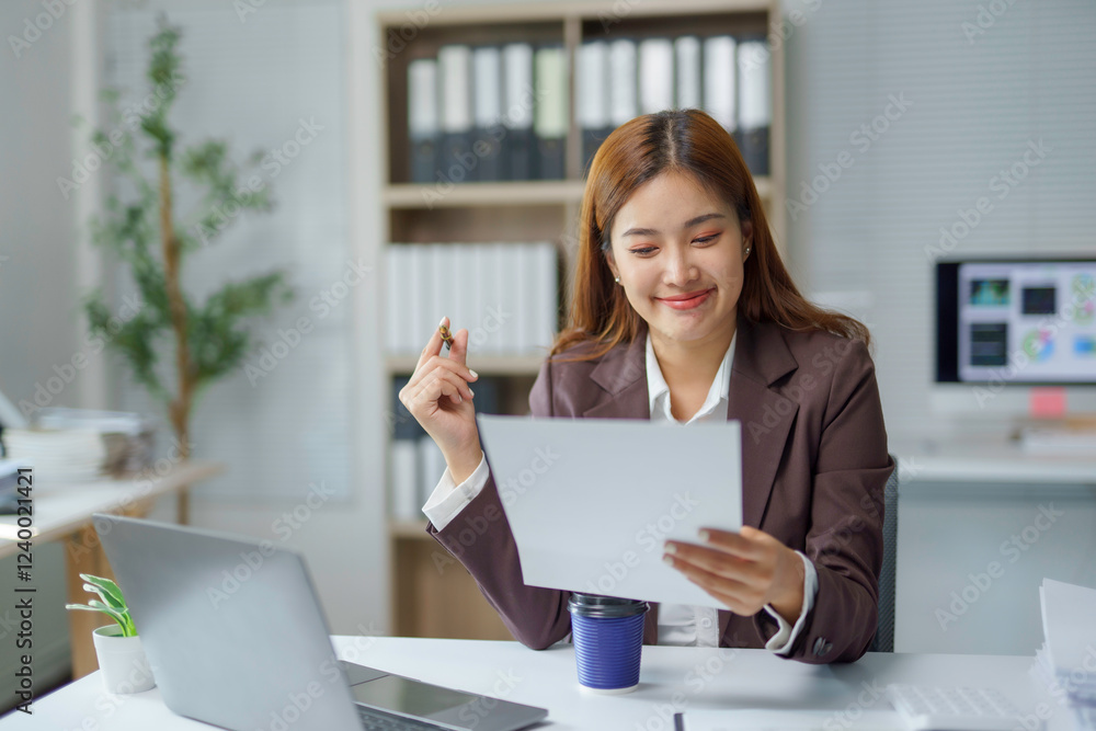 Asian businesswoman smiling and reviewing documents at office desk Asian businesswoman smiling and reviewing documents at office desk