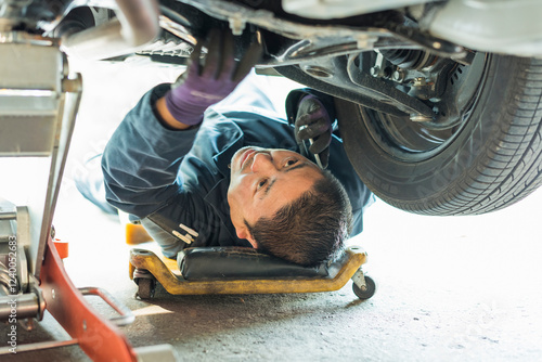 車両の下でメンテナンス作業をする40代男性整備士 photo