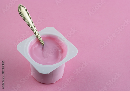 Pink yogurt cup with spoon on pink background