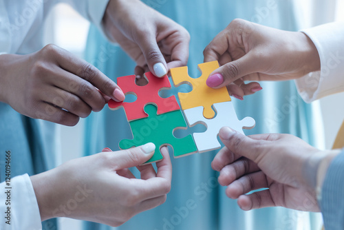 Diverse hands connecting colorful puzzle pieces, symbolizing teamwork and problem-solving. Highlights skin tone diversity and collaboration against a softly blurred neutral background