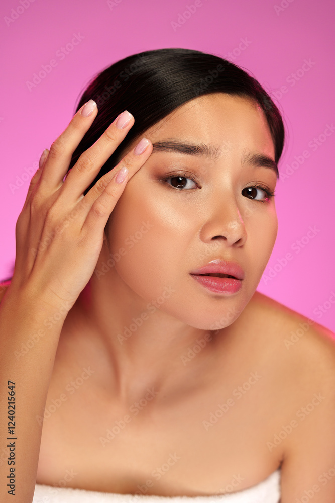 Woman applying skincare product while looking at camera with pink background during a beauty routine Woman applying skincare product while looking at camera with pink background during a beauty routine