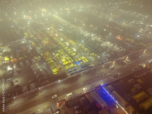 Drone view of Mahakumbh tent city at night, wrapped in fog with glowing tents. A mystical and breathtaking scene showcasing the world's largest spiritual gathering. photo