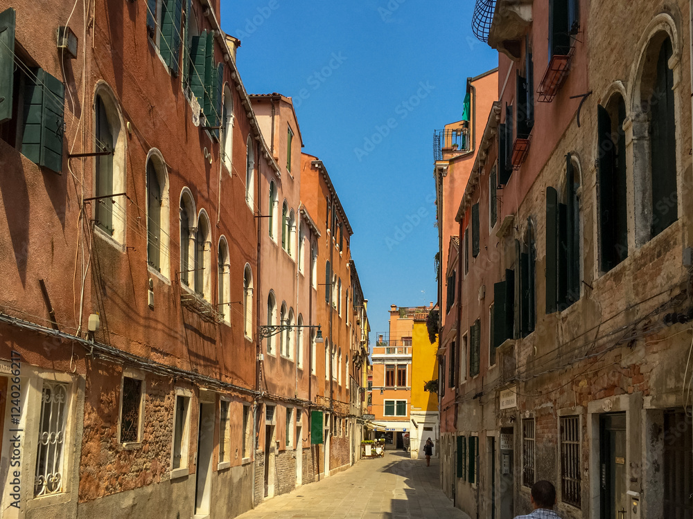 A Narrow Venetian Alleyway. A narrow alleyway winds its way through the city, lined with colorful buildings that lean in towards each other. A Narrow Venetian Alleyway. A narrow alleyway winds its way through the city, lined with colorful buildings that lean in towards each other.
