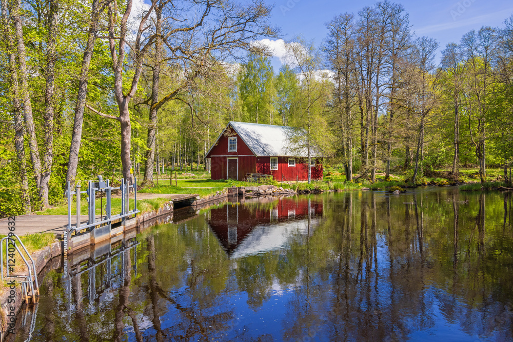 Obraz premium Water dam with a red barn and reflections in the water a sunny spring day