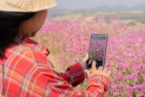 Back view of cropped unrecognizable female tourist taking photo of mountain and field of flowers photo