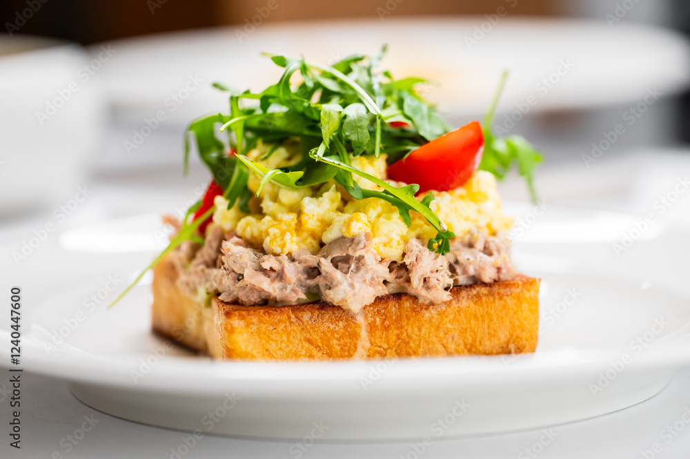 Delicious open-faced sandwich featuring a layer of creamy tuna mixed with herbs, topped with fluffy scrambled eggs, fresh arugula, and a slice of tomato, all served on crusty toasted bread. Delicious open-faced sandwich featuring a layer of creamy tuna mixed with herbs, topped with fluffy scrambled eggs, fresh arugula, and a slice of tomato, all served on crusty toasted bread.