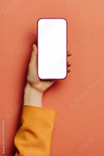 woman's hand in a yellow blazer holds a mobile phone with a white screen mockup against a pink background