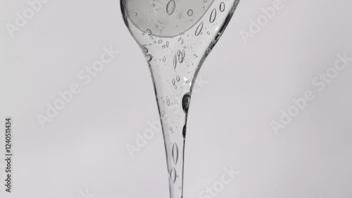 Hyaluronic gel slowly flows from a cosmetic spatula, light gray background.